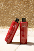 Two red bottles of Oak Professional shampoo and conditioner on a rocky surface.