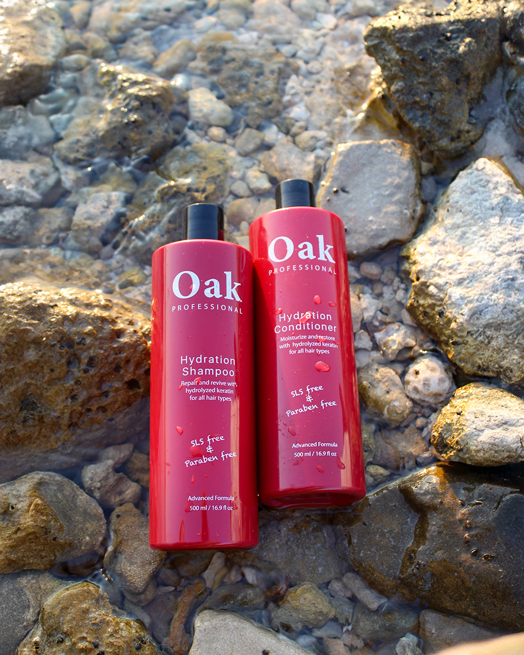 Two red bottles of Oak Professional shampoo and conditioner on a rocky surface.