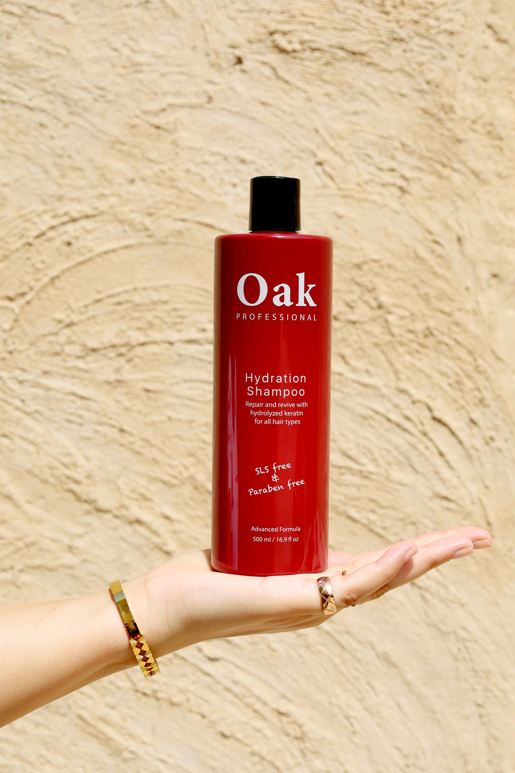 Red shampoo bottle labeled 'Oak' held in a hand against a beige background