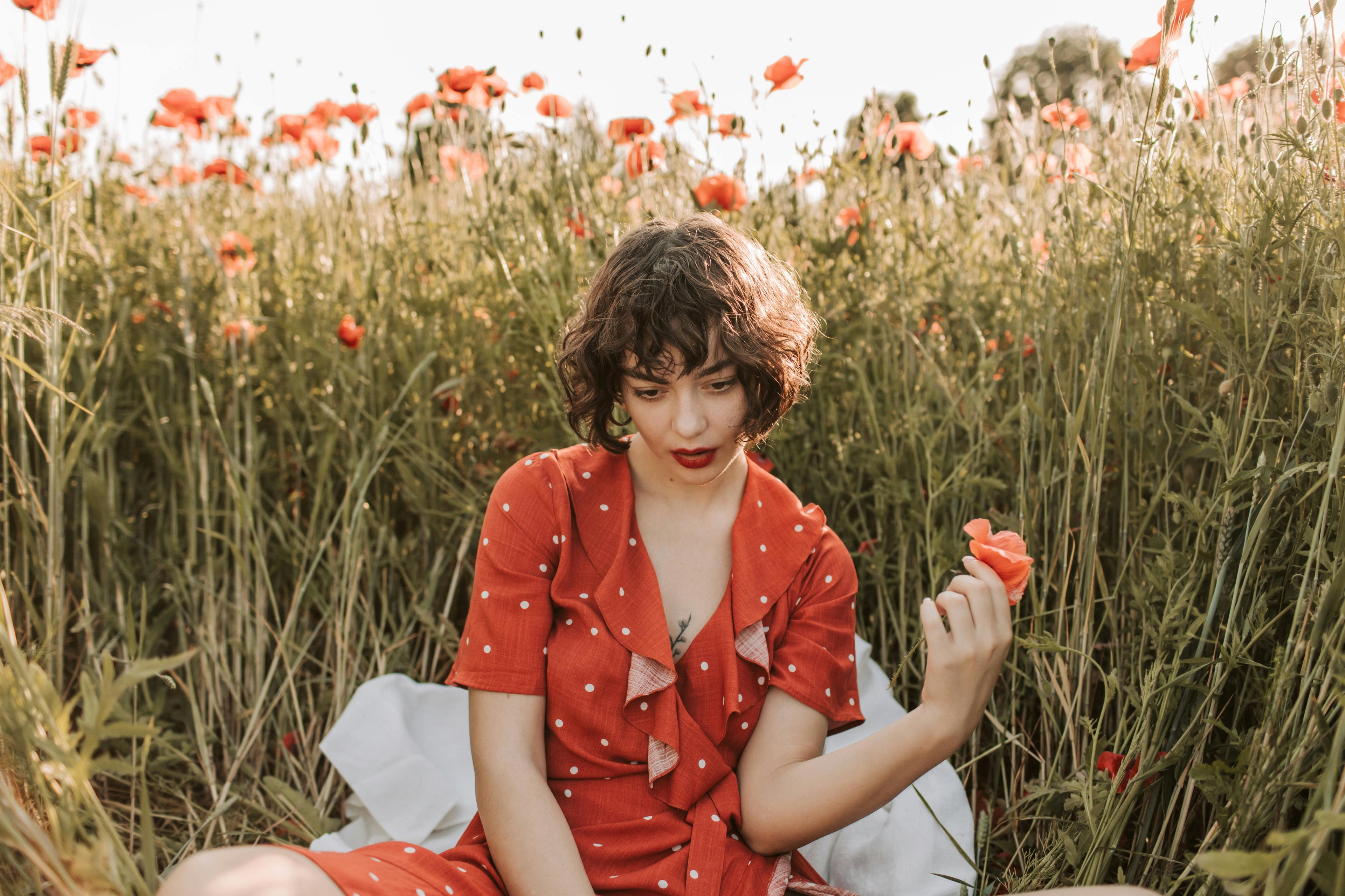 Woman in a red dress sitting among poppies in a field