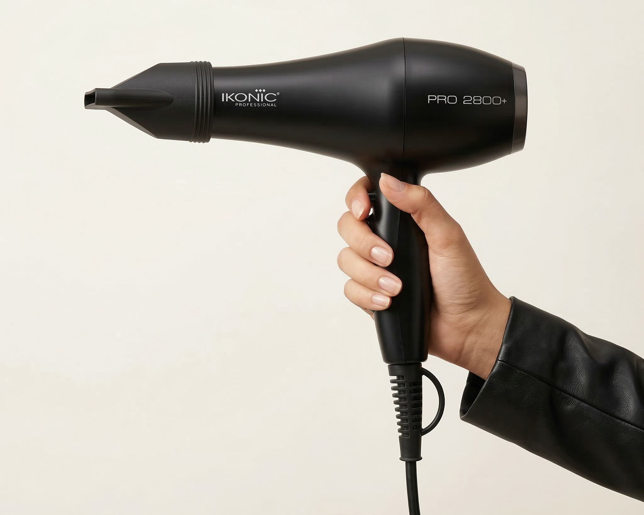 Black hair dryer held by a hand on a beige background